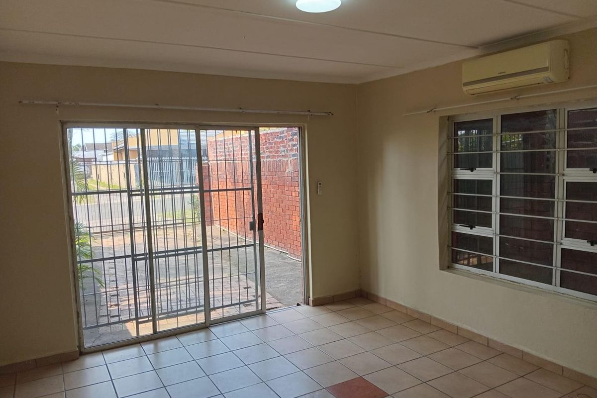 An empty living room featuring tiled flooring, a sliding glass door with security bars, and a wall-mounted air conditioning unit.