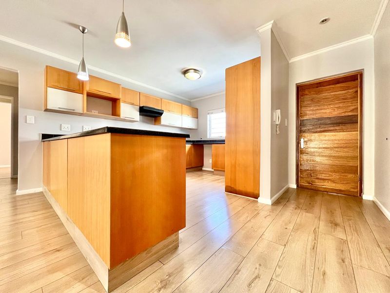 A clean, empty kitchen featuring light wood cabinetry, black granite countertops, laminate flooring, and modern pendant lighting, offering a functional and well-maintained workspace.