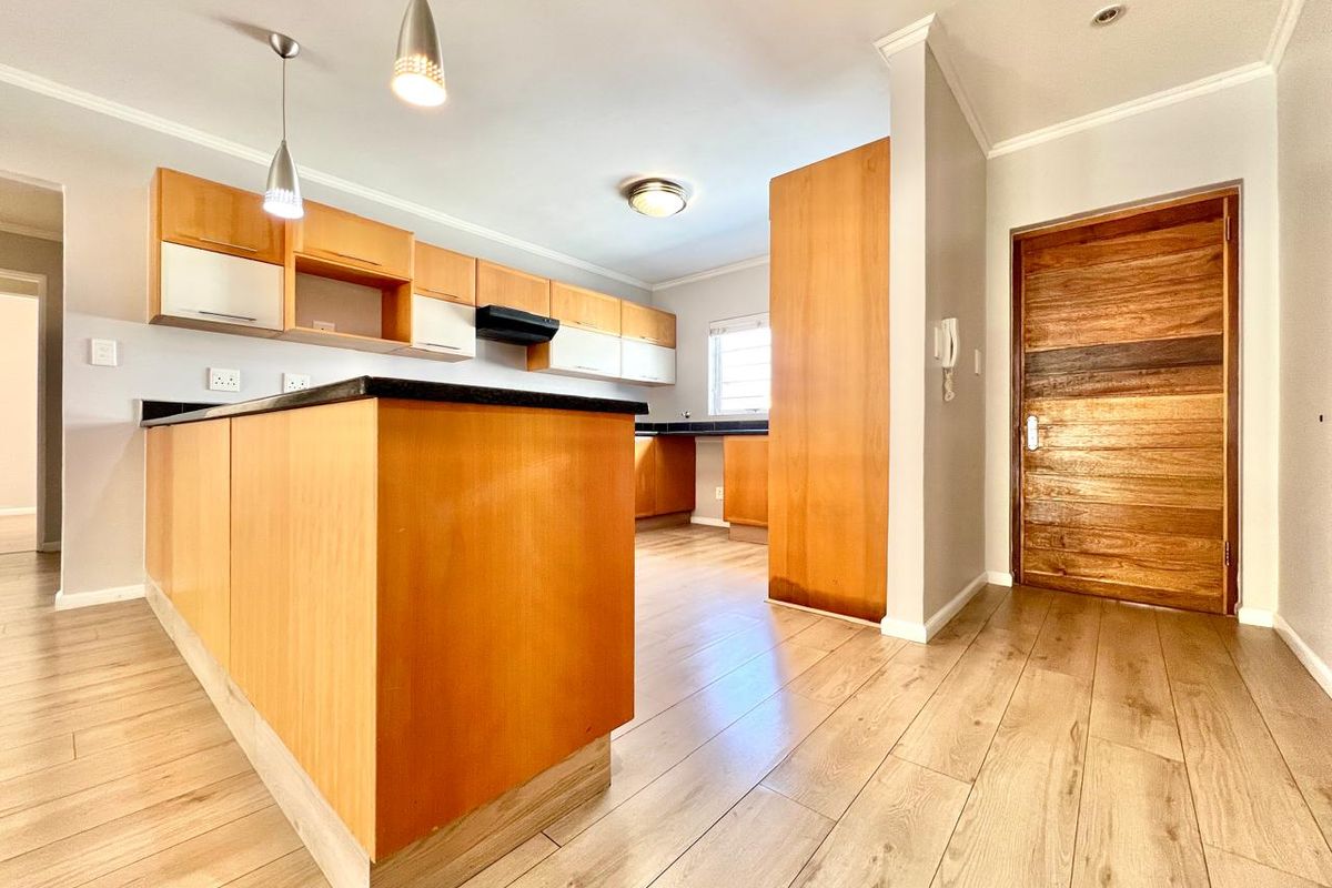 A clean, empty kitchen featuring light wood cabinetry, black granite countertops, laminate flooring, and modern pendant lighting, offering a functional and well-maintained workspace.