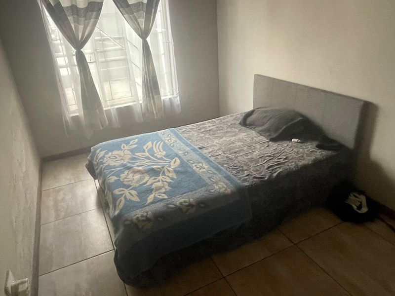 A simple bedroom featuring tiled flooring and a window with security bars, providing natural light.