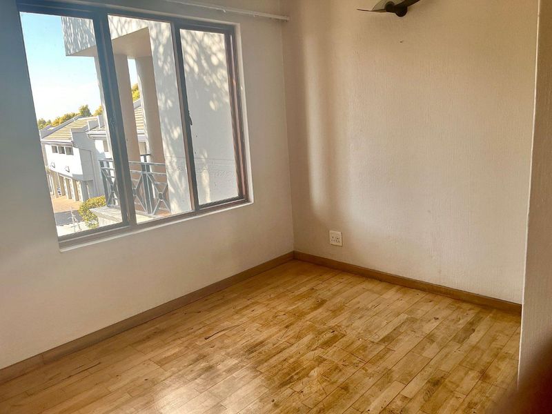 An empty bedroom featuring laminate flooring, neutral walls, and a large window providing natural light and views of the surrounding townhouse complex.