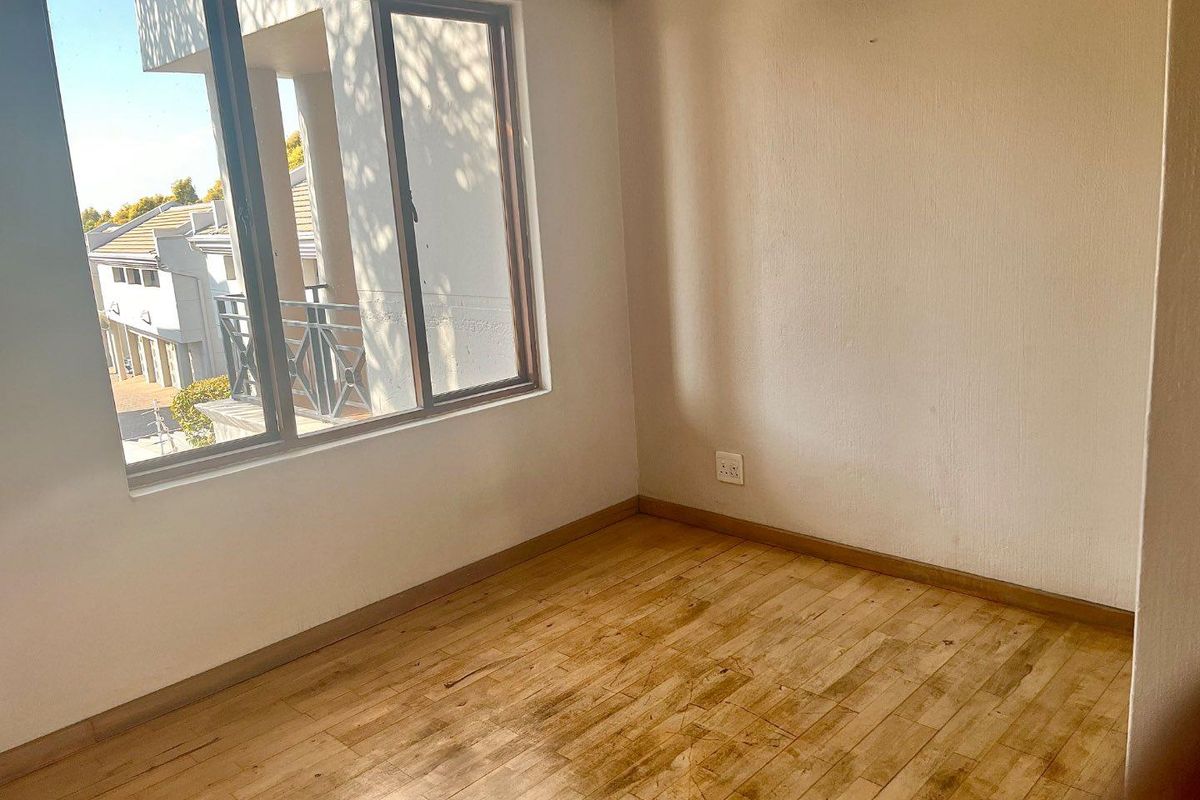 An empty bedroom featuring laminate flooring, neutral walls, and a large window providing natural light and views of the surrounding townhouse complex.