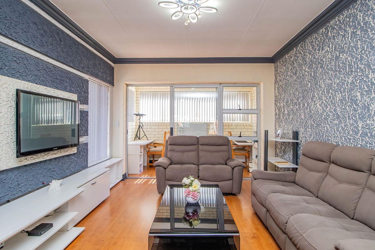 A living room featuring laminate flooring, textured accent walls, crown molding, and sliding glass doors leading to an enclosed patio area.