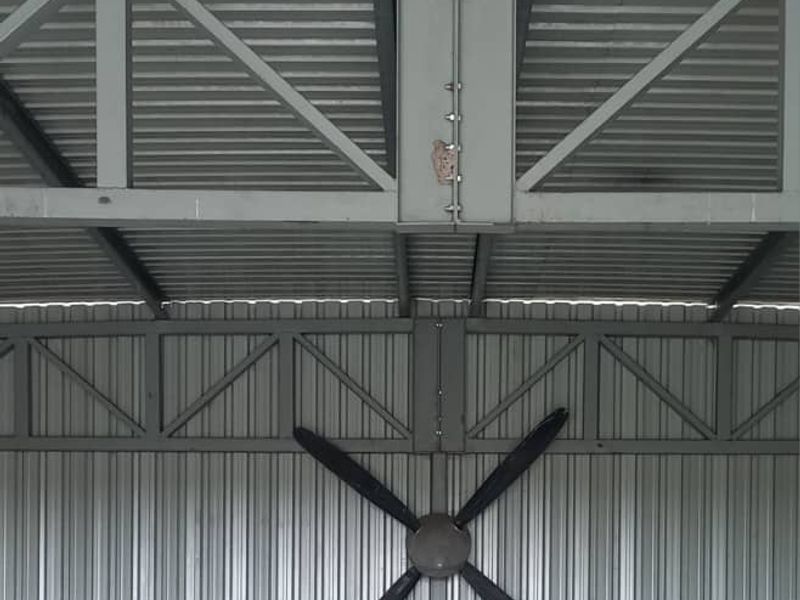 A large, open-plan industrial-style shed or garage featuring exposed steel trusses and corrugated metal wall cladding.