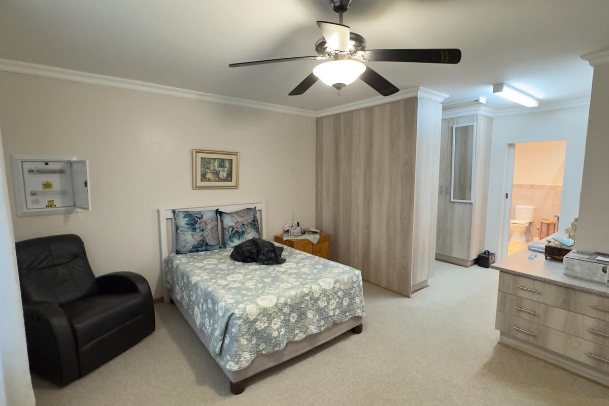 Spacious bedroom featuring built-in cabinetry, a ceiling fan, and an en-suite bathroom access.