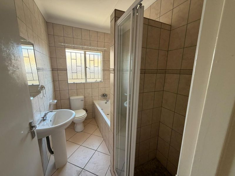 A functional bathroom featuring a pedestal basin, toilet, built-in bathtub, and a separate shower enclosure with full-height wall tiling.