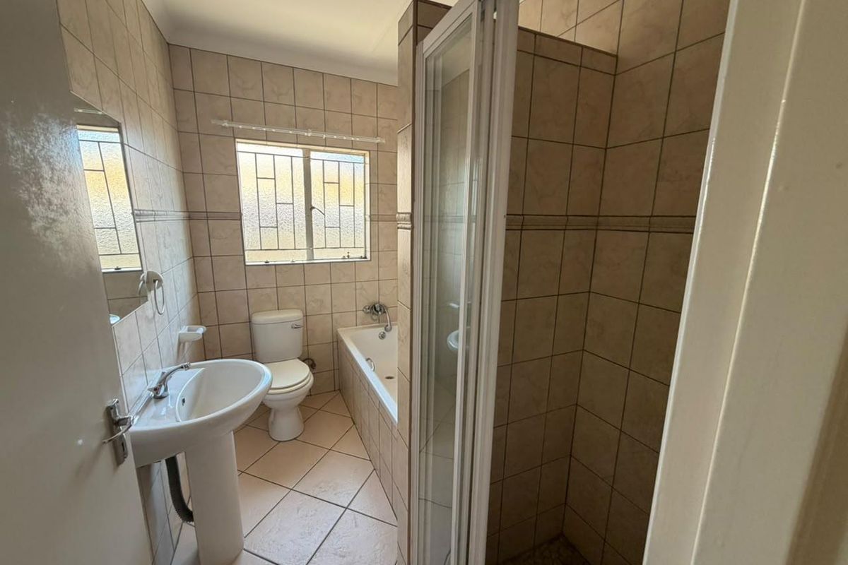 A functional bathroom featuring a pedestal basin, toilet, built-in bathtub, and a separate shower enclosure with full-height wall tiling.