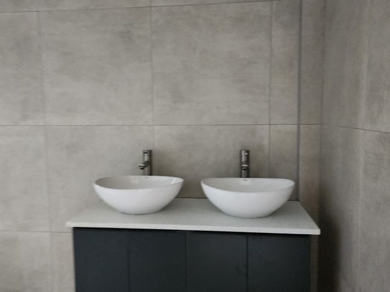 Modern bathroom featuring a double vanity with vessel sinks, wall-mounted faucets, and contemporary large-format grey wall tiling.