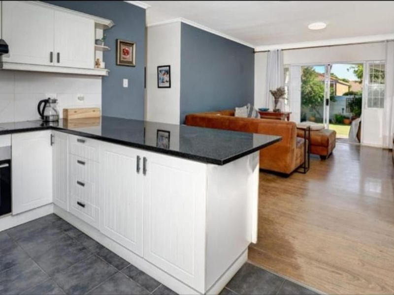 Open-plan kitchen and living area featuring white cabinetry, granite countertops, and sliding doors leading to the rear garden.