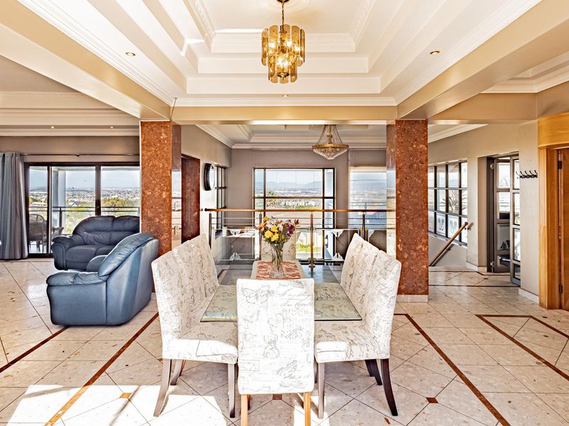 Spacious open-plan living and dining area featuring elegant marble flooring, coffered ceilings, stone-clad columns, and expansive views through large sliding glass doors.