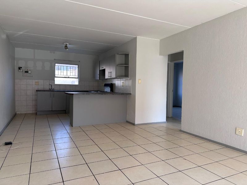 An open-plan living and kitchen area featuring tiled flooring, built-in cabinetry, and a breakfast counter, currently vacant and awaiting finishing touches.