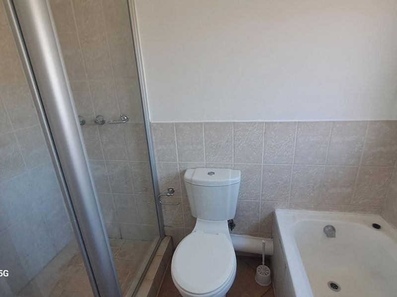 A functional bathroom featuring a shower enclosure, a bathtub, and a toilet with neutral wall tiling.