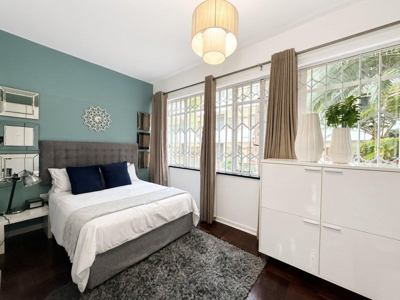 A well-maintained bedroom featuring hardwood flooring, large windows with security bars, and a feature wall.