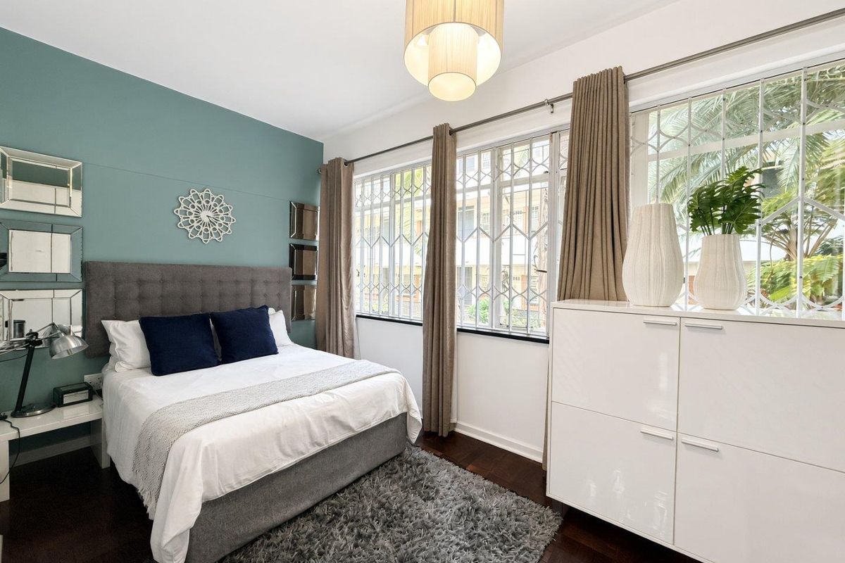 A well-maintained bedroom featuring hardwood flooring, large windows with security bars, and a feature wall.