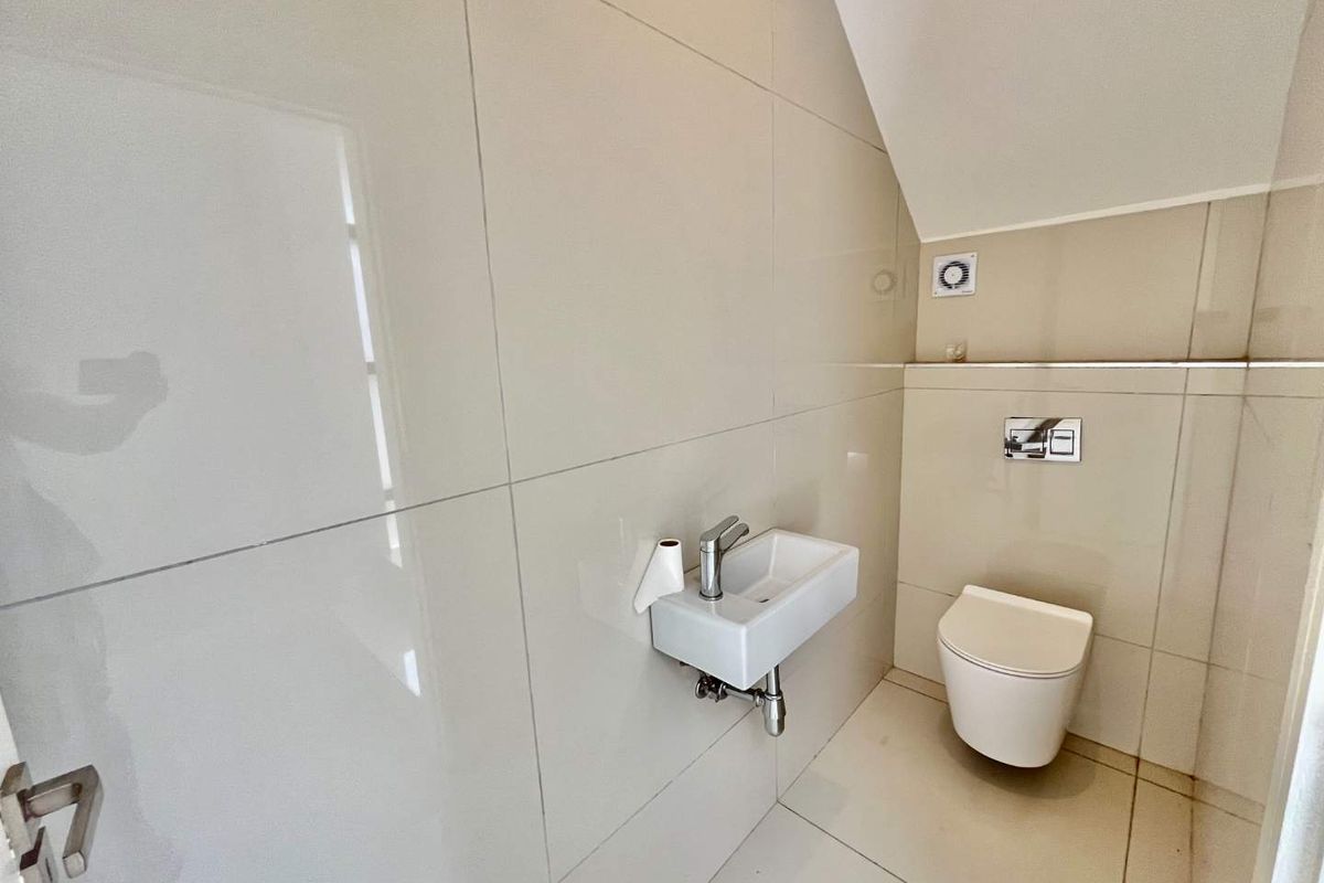 A compact, modern guest bathroom featuring large-format wall tiles, a wall-mounted toilet with a concealed cistern, and a small wall-hung basin.