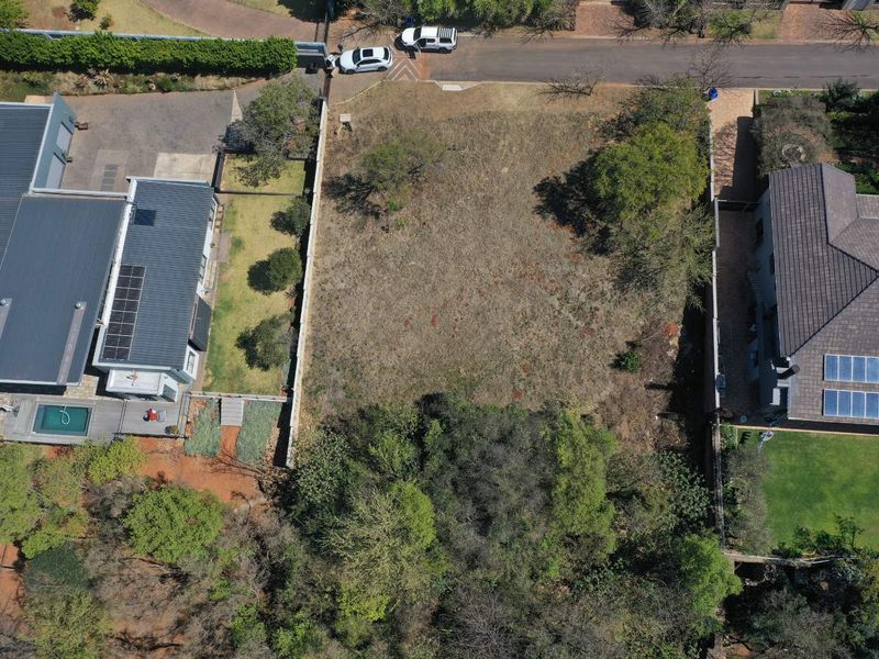 An aerial view of a vacant residential plot situated between two existing properties, featuring established boundary walls and natural vegetation.