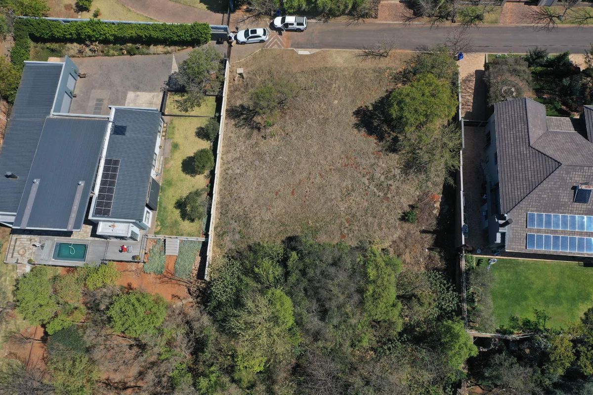 An aerial view of a vacant residential plot situated between two existing properties, featuring established boundary walls and natural vegetation.