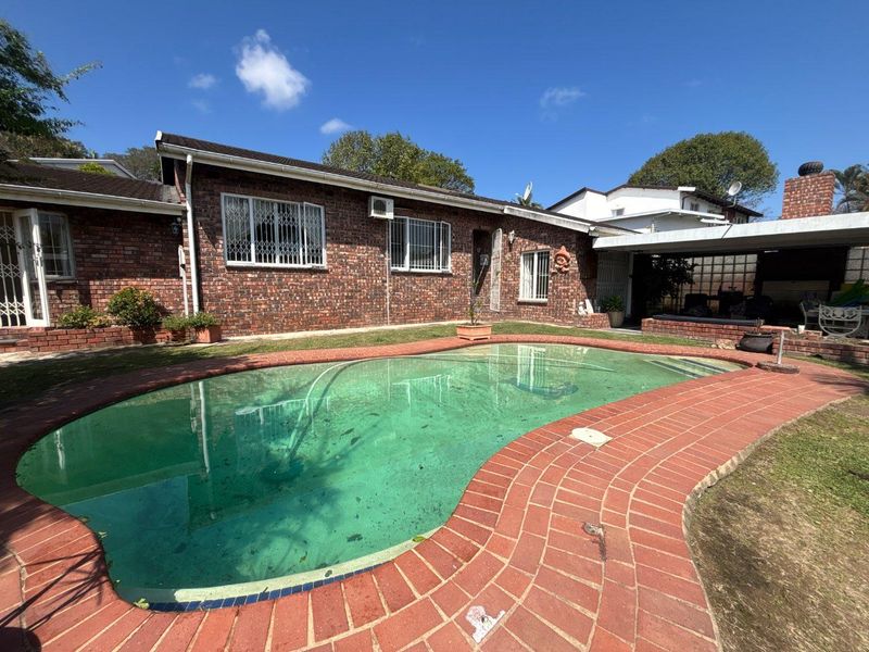 Rear exterior view featuring a swimming pool with brick surround, brick facade house, and a covered patio area.