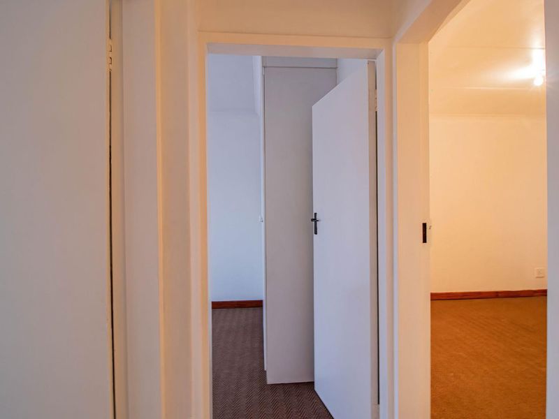 A view through a hallway connecting multiple rooms, featuring neutral walls, carpeted flooring, and built-in storage cupboards.