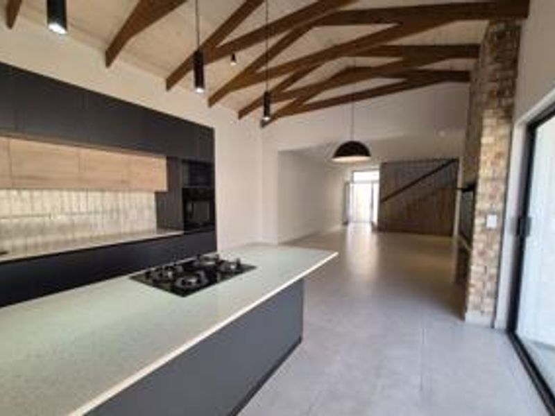 Modern open-plan living area featuring a sleek kitchen with island, gas hob, exposed timber beams, and large sliding doors leading to the exterior.