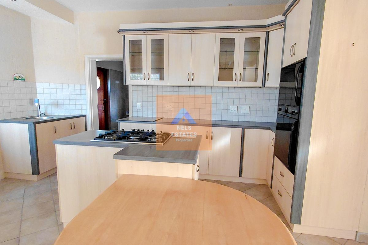 A functional kitchen featuring light-toned cabinetry, a central island with a gas hob, built-in oven, and tiled backsplash with ample counter space.
