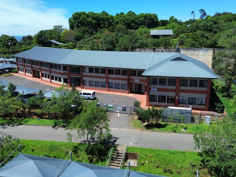 Aerial view of a multi-story office building featuring a metal roof, brick facade, paved driveway, and extensive covered parking facilities within a landscaped setting.