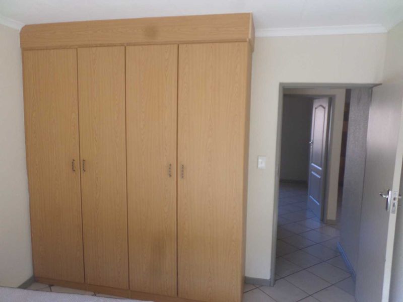 A bedroom featuring built-in wooden cupboards and tiled flooring, leading into a hallway with additional door access.