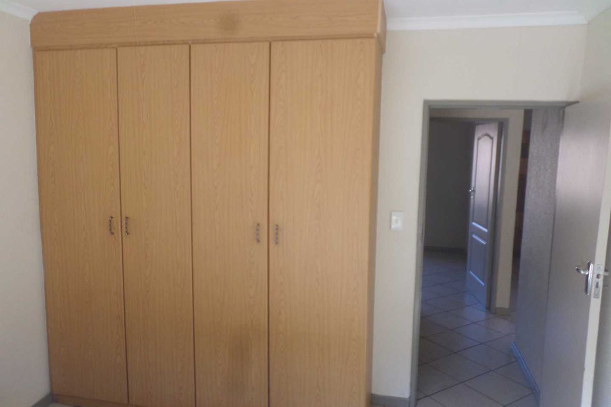 A bedroom featuring built-in wooden cupboards and tiled flooring, leading into a hallway with additional door access.