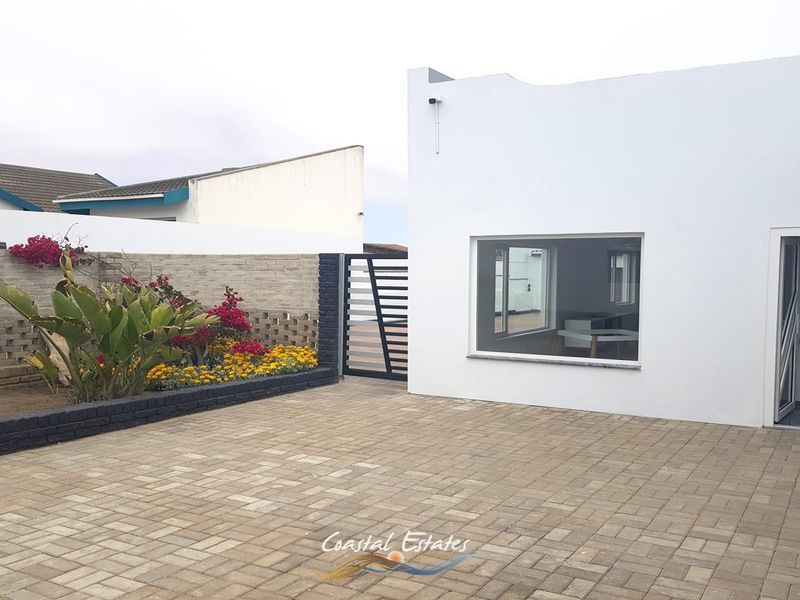 A clean, paved rear courtyard area featuring a raised garden bed, secure boundary wall, and modern exterior finishes.