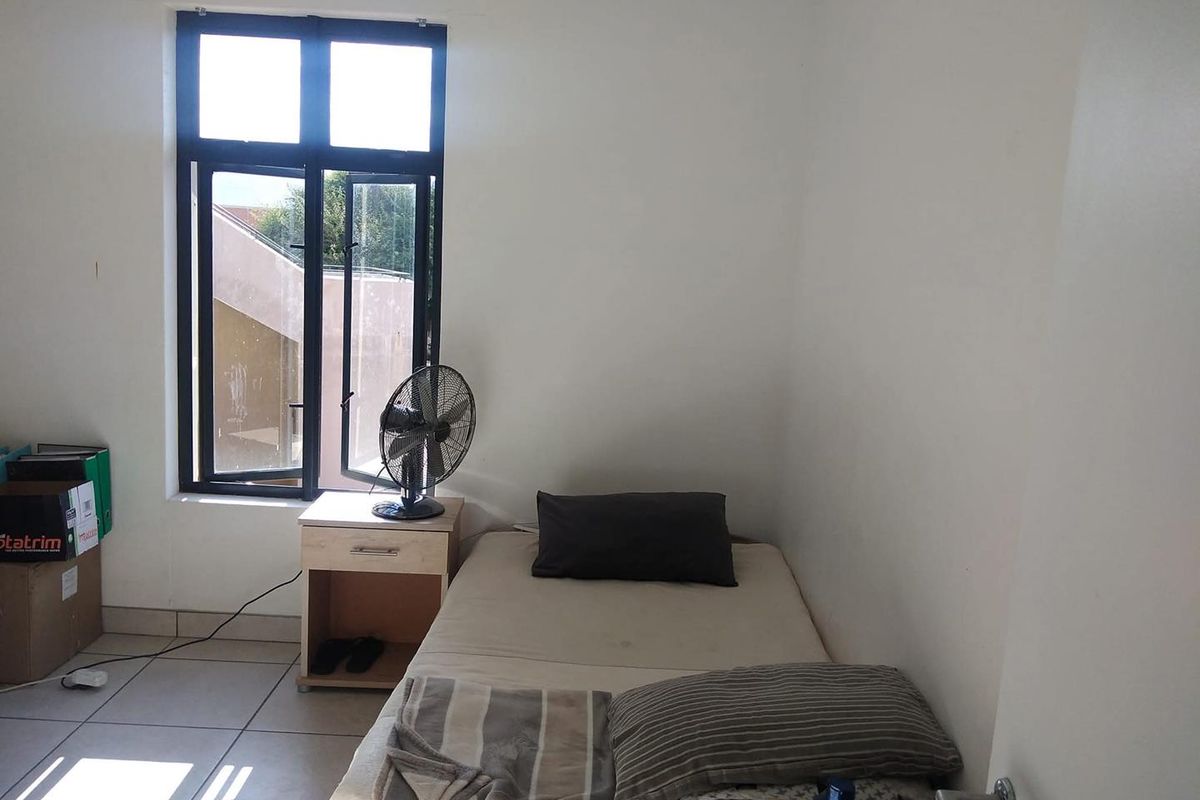 A simple bedroom featuring tiled flooring and a window providing natural light.