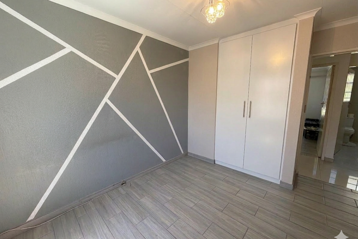 A bright, empty bedroom featuring modern grey geometric wall accents, built-in wardrobes, and contemporary tiled flooring.