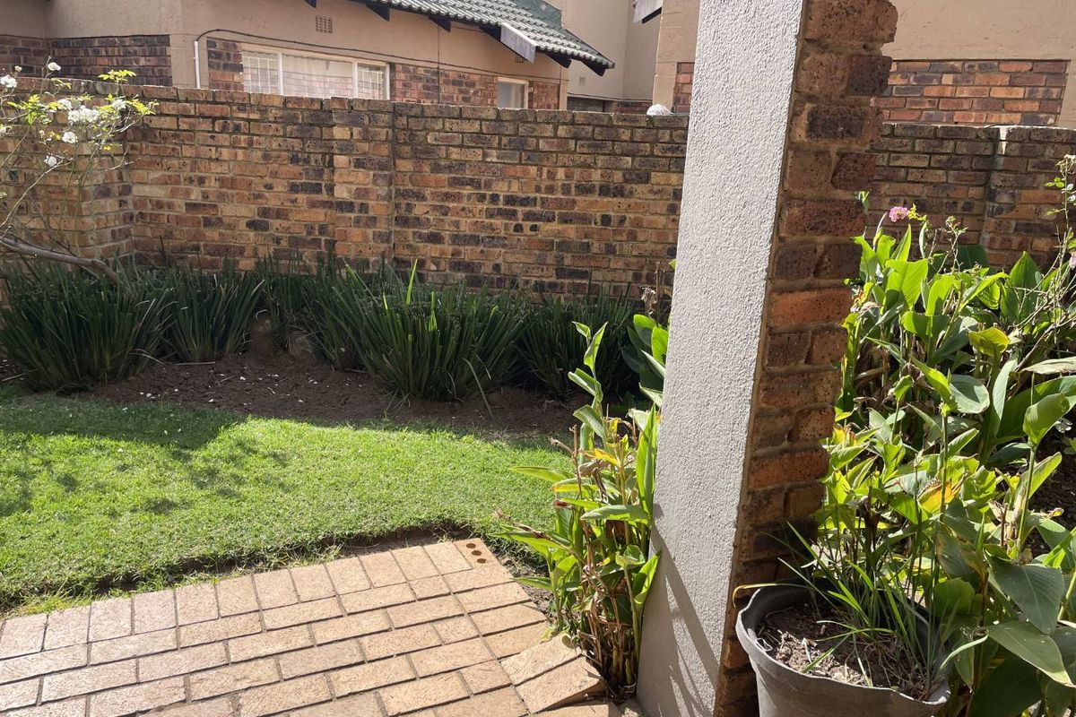 A private rear garden area featuring a paved patio, a small lawn, and a brick boundary wall.