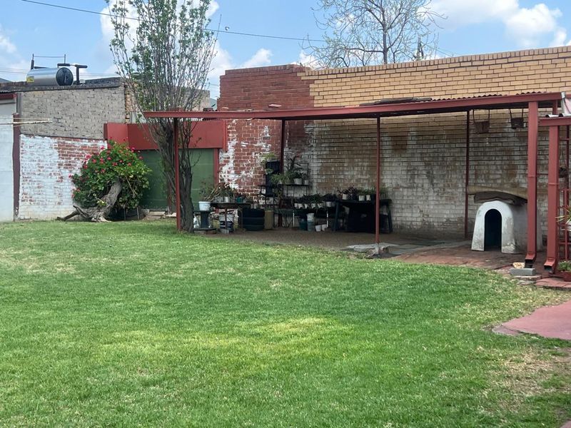 Rear garden area featuring a lawn and a covered patio structure against a weathered brick boundary wall.