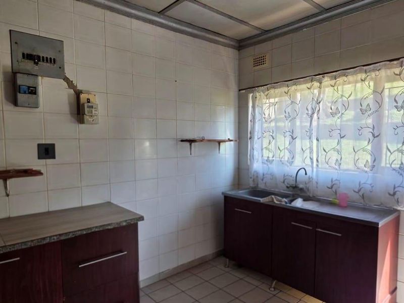 A functional kitchen featuring dark cabinetry, tiled splashbacks, and direct access to the rear garden area.