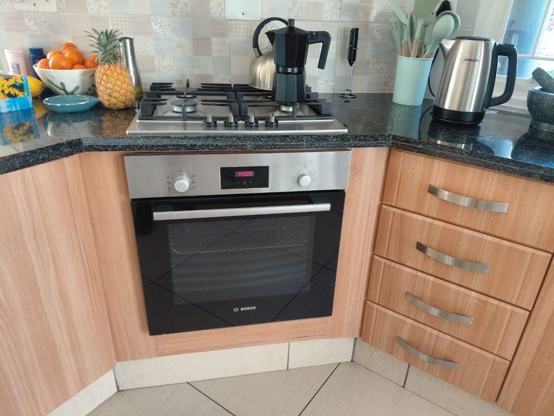 A functional kitchen corner featuring a built-in Bosch oven, gas cooktop, granite countertops, and light wood-finish cabinetry with a tiled backsplash.