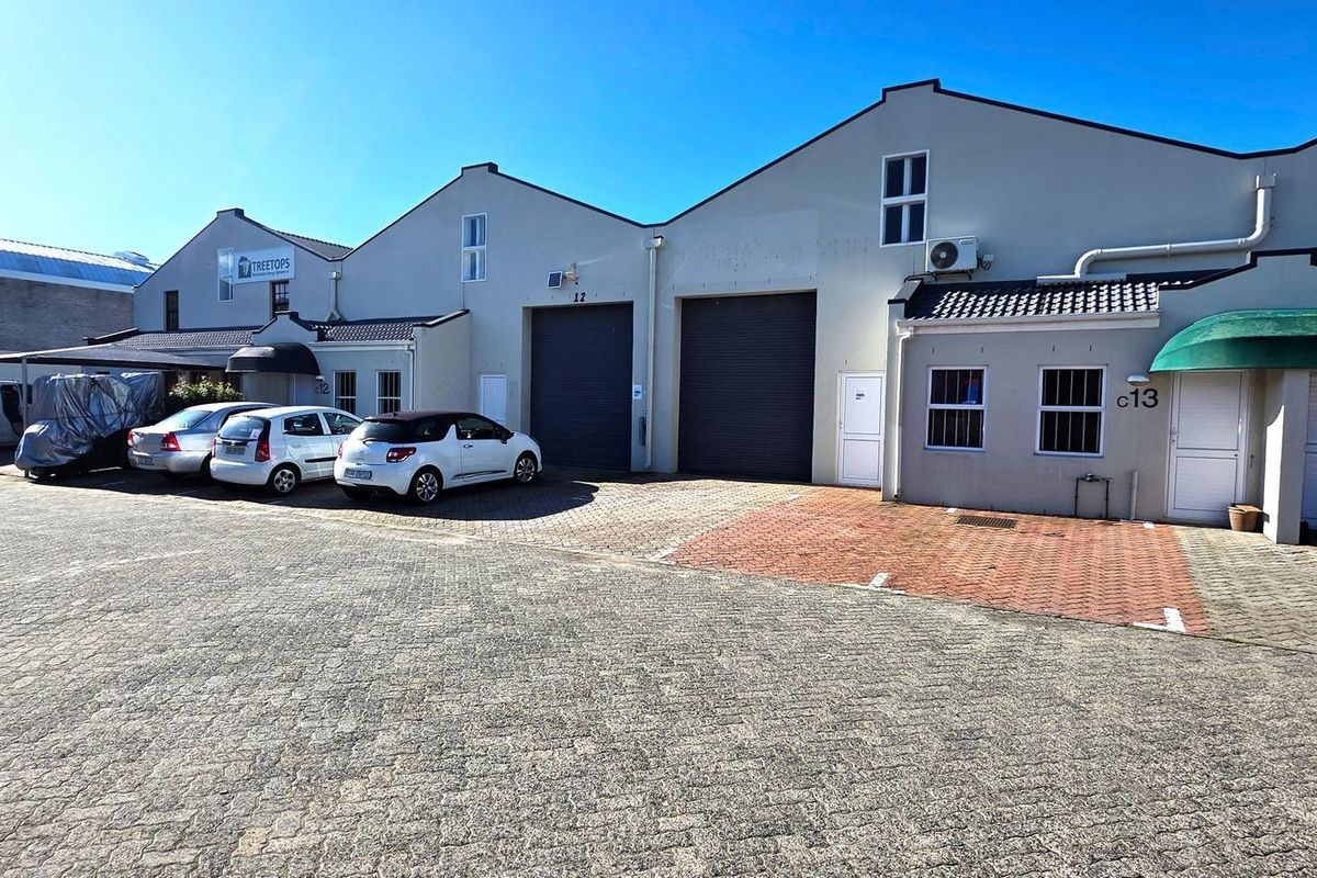 Front elevation of an industrial complex featuring multiple roller shutter doors, paved parking area, and professional building finishes.