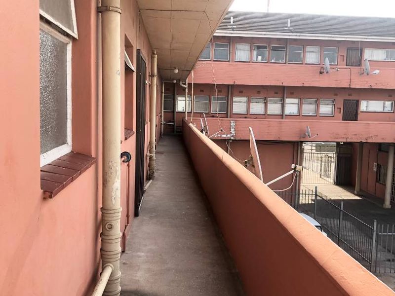 An exterior concrete balcony walkway featuring exposed plumbing pipes and metal railings, overlooking the townhouse complex courtyard.