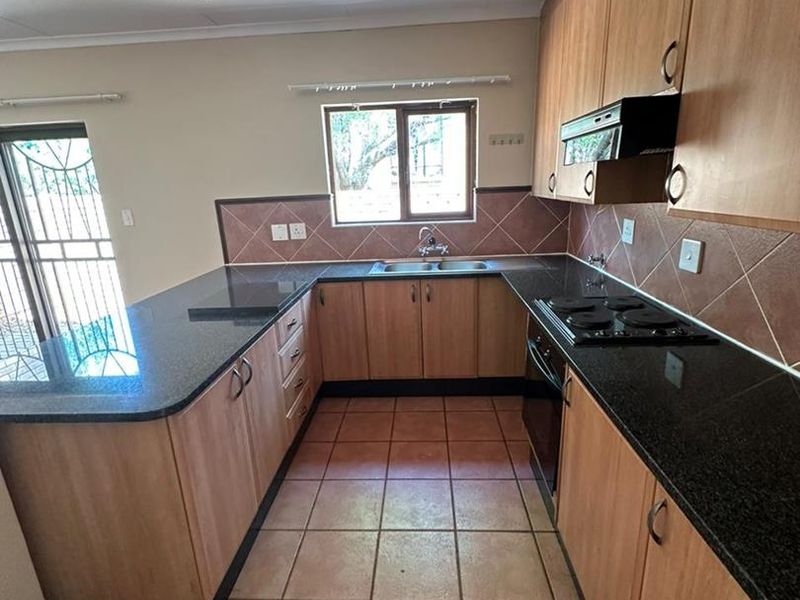 A functional kitchen featuring laminate cabinetry, granite countertops, built-in electric hob and oven, and tiled flooring with direct access to an outdoor area.
