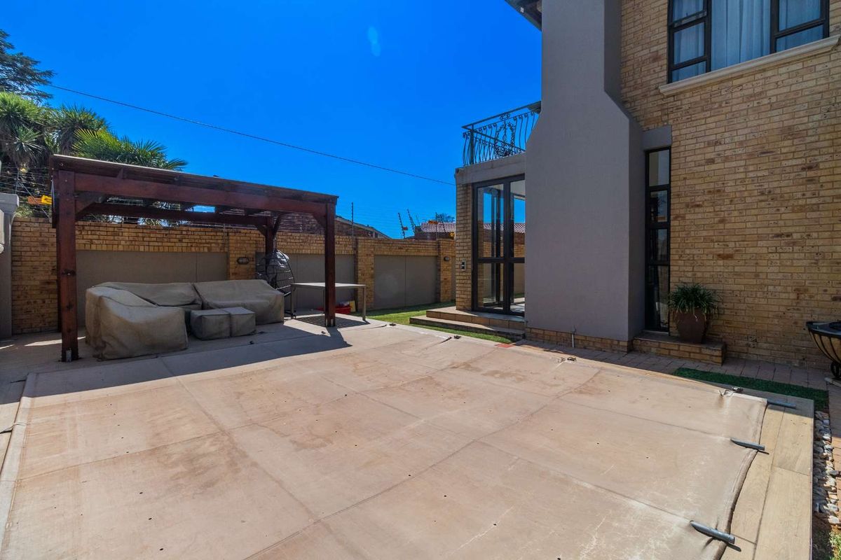 Rear exterior view featuring a paved patio area, a wooden pergola, and a swimming pool with a safety cover, adjacent to the main house structure.