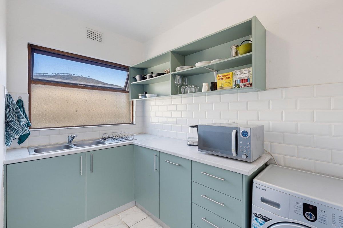A functional kitchen featuring sage green cabinetry, white subway tile backsplash, laminate countertops, and a double sink with natural light.