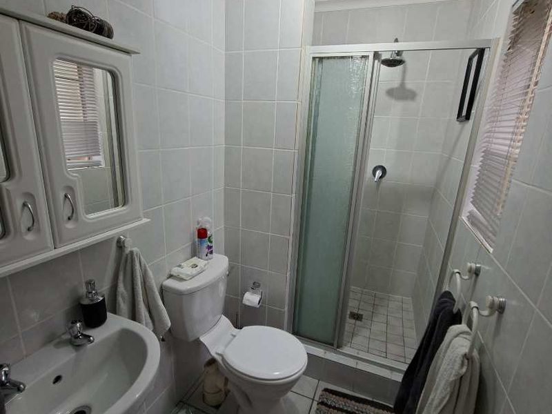 A functional bathroom featuring a pedestal sink, a built-in shower enclosure, and a toilet, finished with neutral wall and floor tiles.