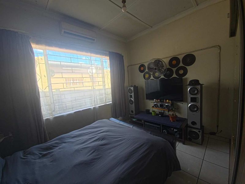 A bedroom featuring tiled flooring, a wall-mounted air conditioning unit, and security bars on the window.