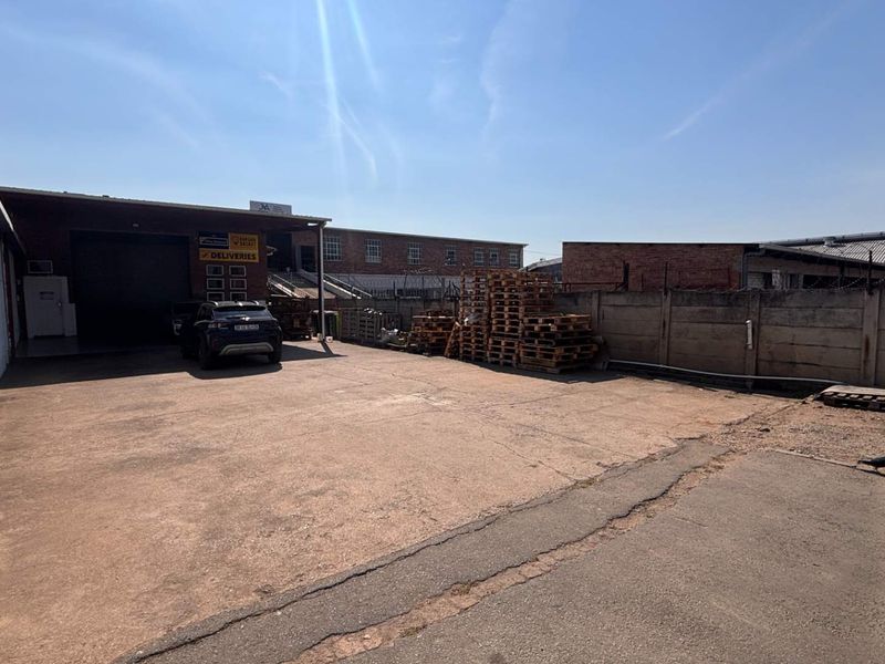 Rear exterior yard area featuring a concrete surface, brick boundary wall with security fencing, and access to a commercial roller shutter door.