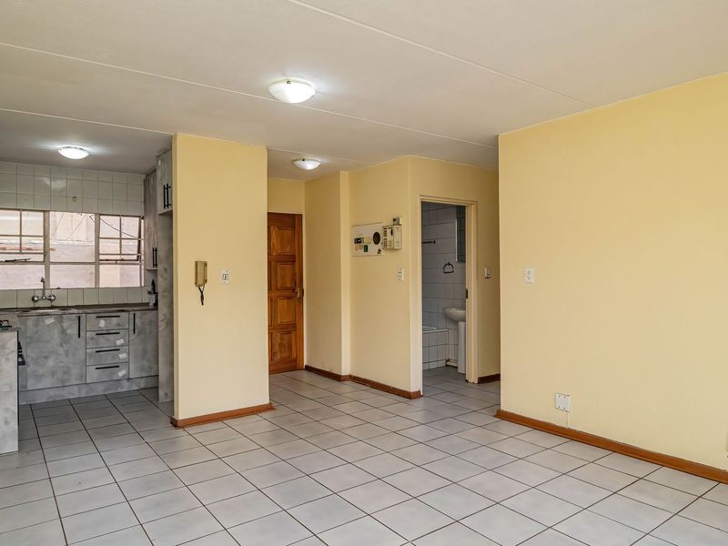 An open-plan living and kitchen area featuring tiled flooring, built-in cabinetry, and direct access to a bathroom, presenting a clean, vacant space.