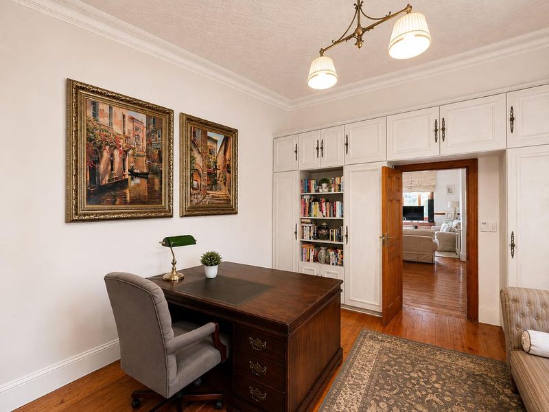A well-maintained home office featuring classic hardwood flooring, extensive built-in storage cabinetry, and elegant crown molding details.