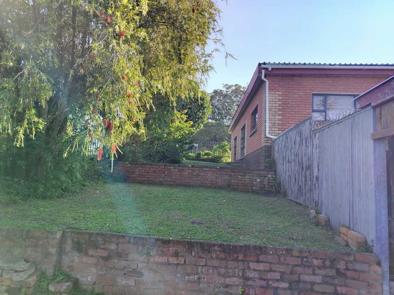 Rear exterior view of the property featuring a brick facade, tiered garden with brick retaining walls, and perimeter fencing.