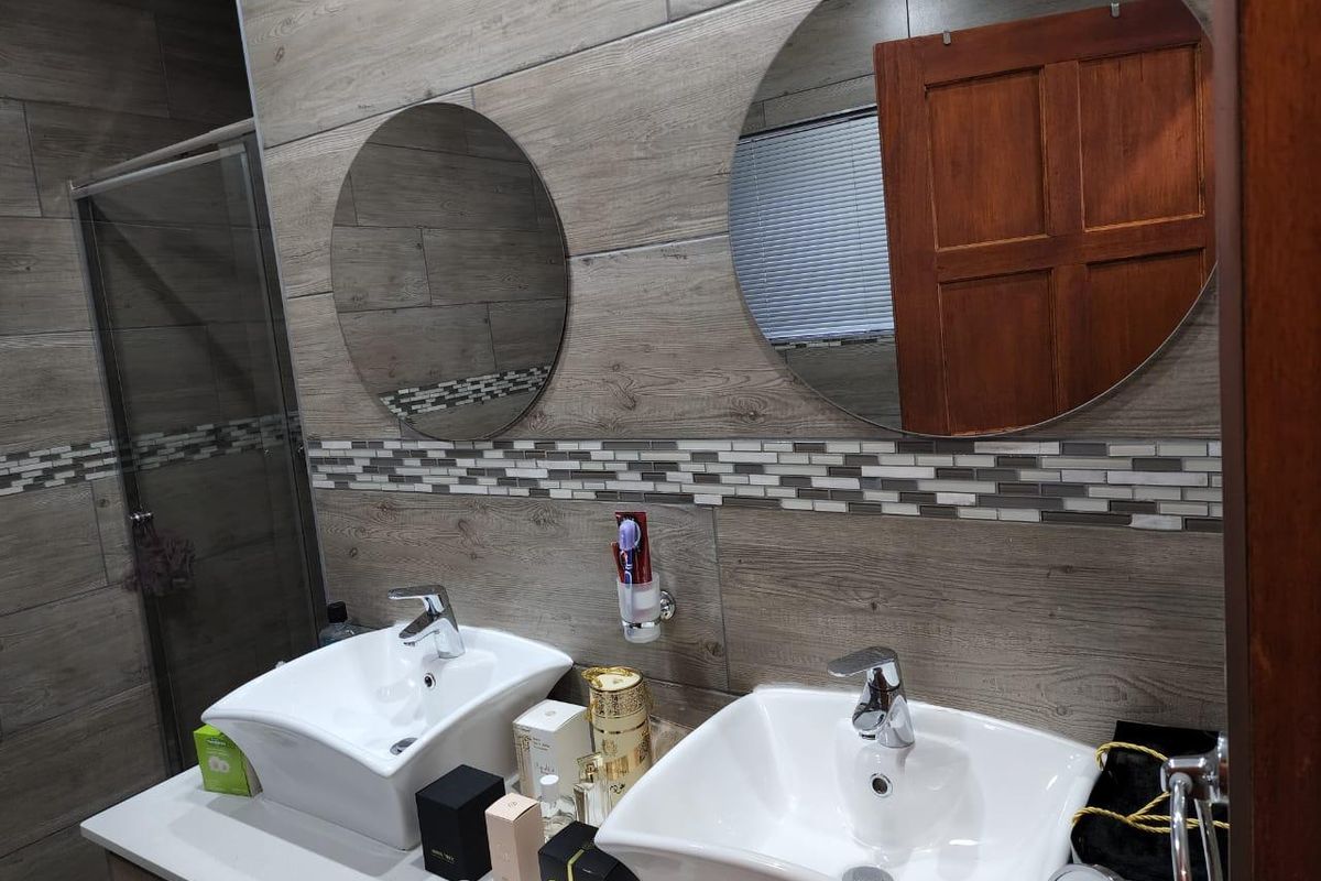 Modern bathroom featuring a double vanity with vessel sinks, wood-look wall tiling, mosaic accents, and a glass-enclosed shower.