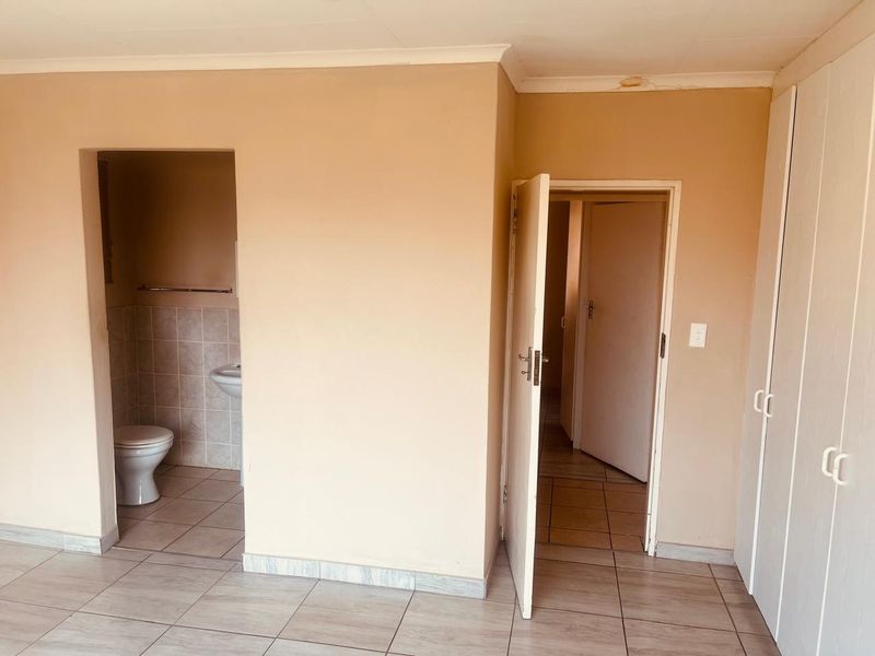 An empty bedroom featuring tiled flooring, built-in cupboards, and an attached en-suite bathroom, requiring minor ceiling repairs and cosmetic updates.