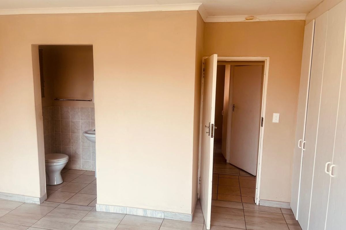 An empty bedroom featuring tiled flooring, built-in cupboards, and an attached en-suite bathroom, requiring minor ceiling repairs and cosmetic updates.