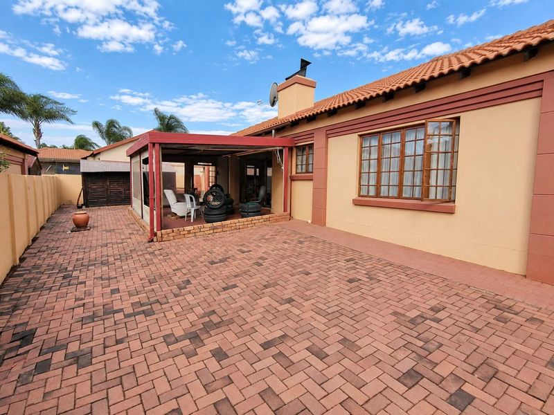 Rear exterior view featuring a paved courtyard, a covered patio area, and a traditional house facade with terracotta roof tiles.